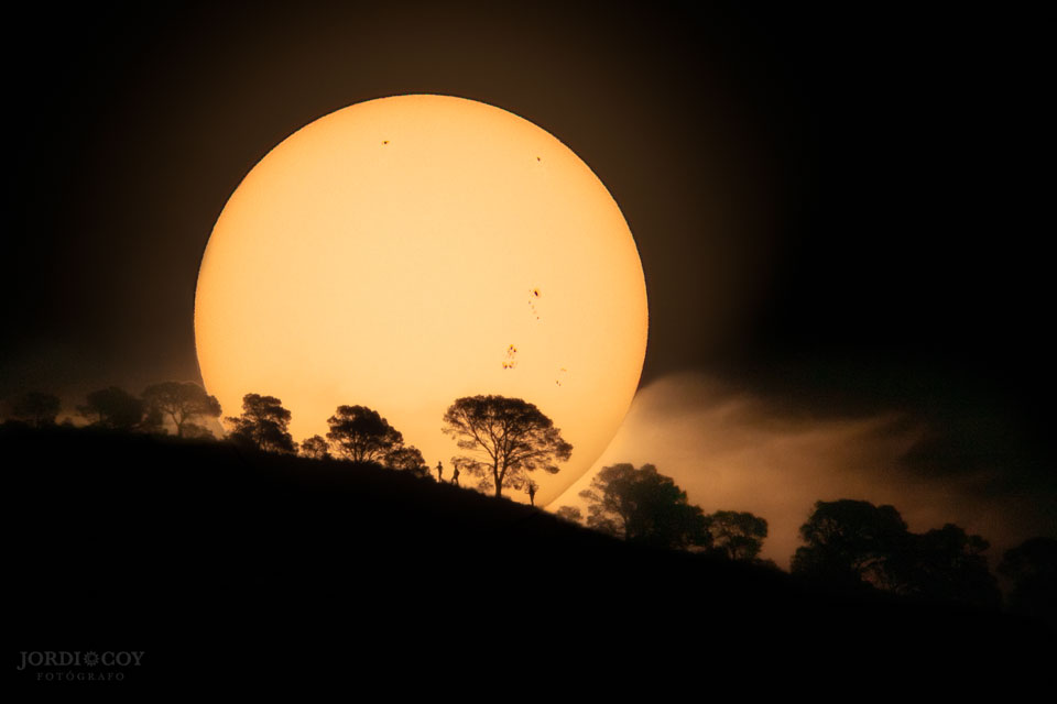 图片显示太阳从西班牙珀特的一座小山上升起，上面有太阳黑子和前景树木。有关更多详细信息，请参阅说明。