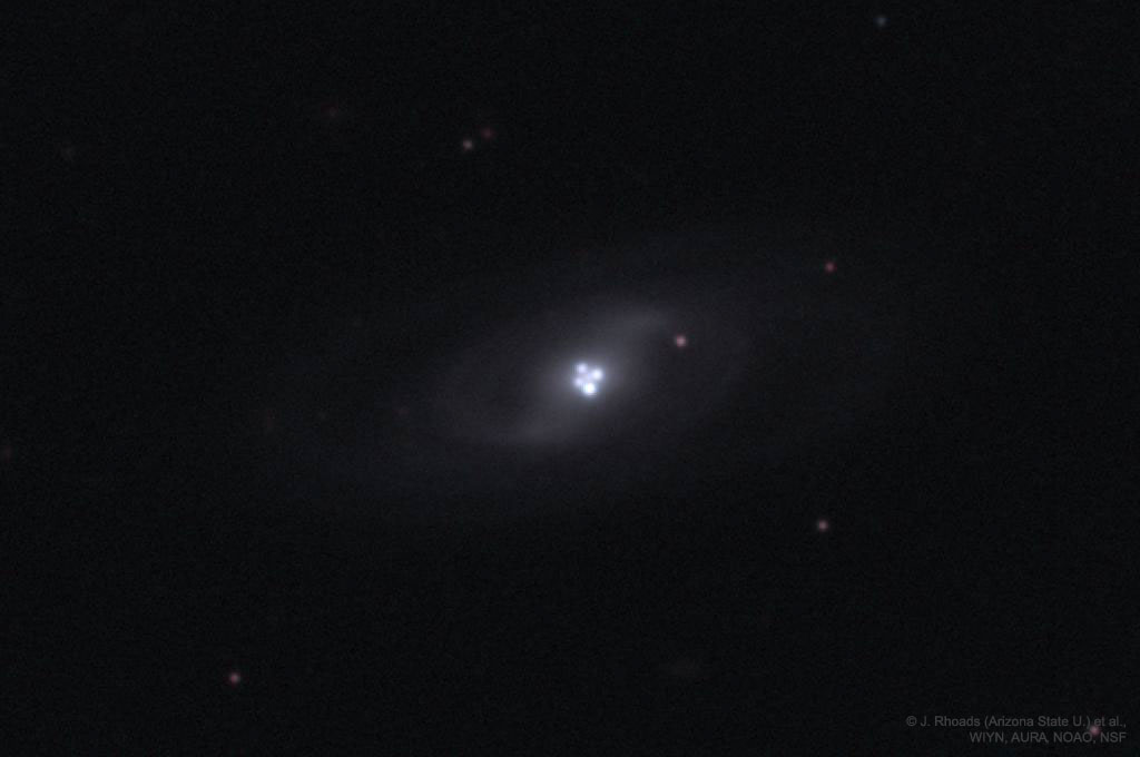 这张图片显示了一个遥远的类星体，由于中间星系的引力透镜效应，它出现了四次。有关更多详细信息，请参阅说明。
