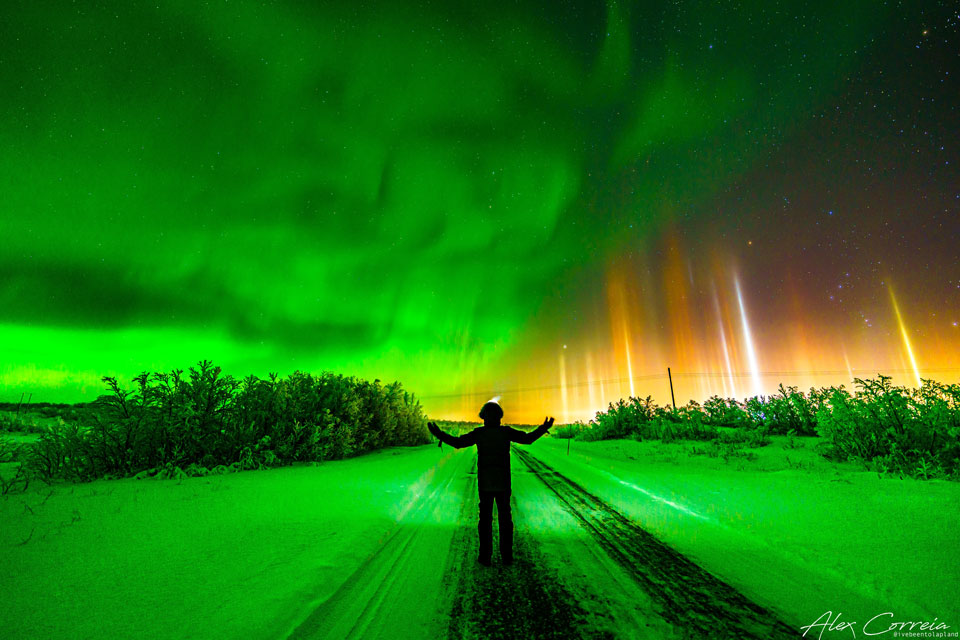 特色图片显示摄影师站在夜空下，左边是绿色的极光，右边是五颜六色的光柱。请参阅说明以获取更多详细信息。