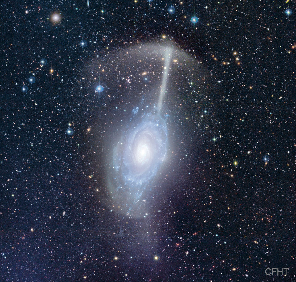 这张特色图片显示了一个被称为雨伞星系的星系合并，因为一个星系的残骸看起来就像一把伞，悬停在另一个星系上空。请参阅说明以获取更多详细信息。