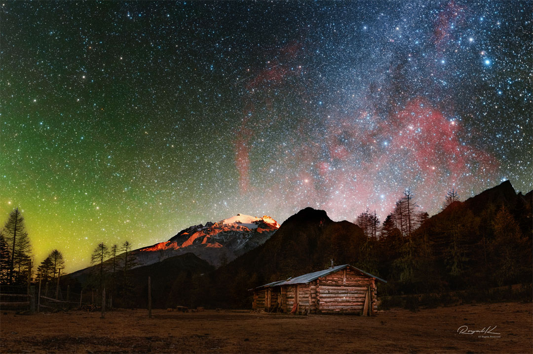 这张特色图片显示了广阔的甘姆星云，在木屋和雪山的风景后面发出红色的光芒。不寻常的光。请参阅说明以获取更多详细信息。