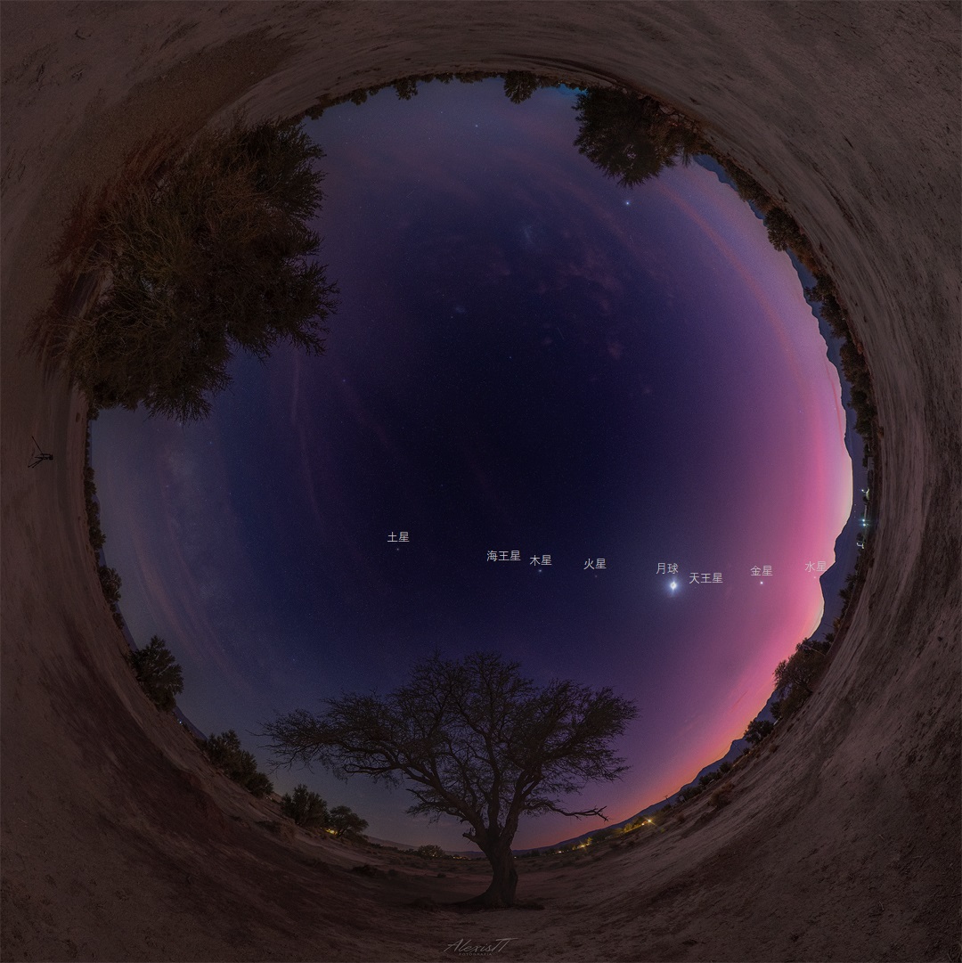 这幅特色图片是一幅圆形鱼眼全天空图像，显示了太阳系中的每一颗行星与地球的卫星沿图像中心水平排列。阿塔卡马沙漠连接的树木和山丘分布在外圈边缘。请参阅说明以获取更多详细信息。