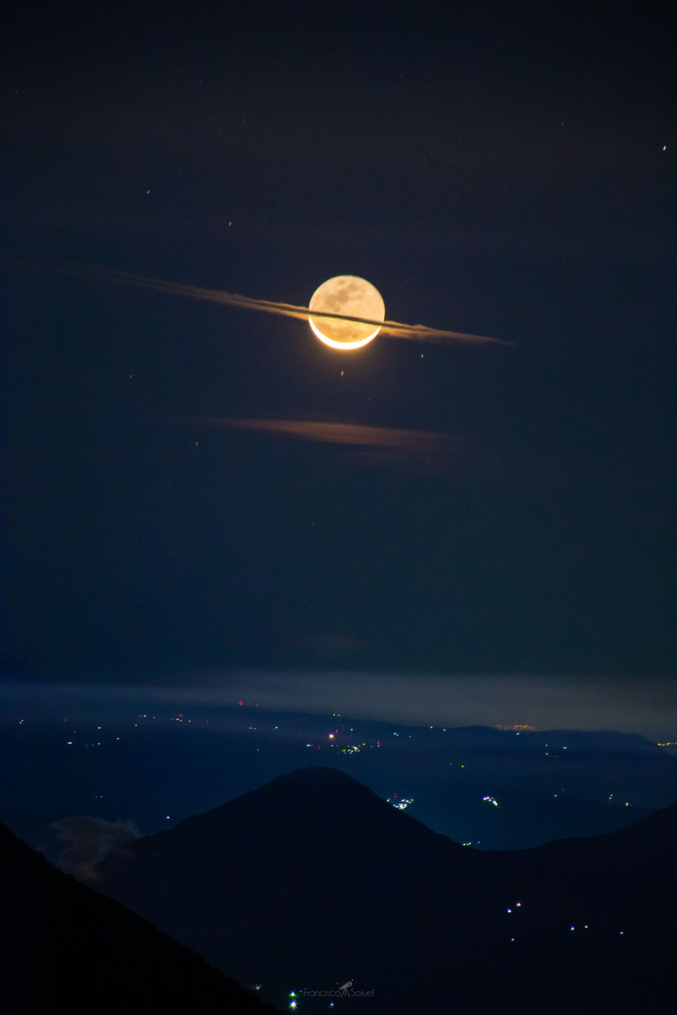 这张特色图片显示，在一座城市和一座火山上空有一轮新月，中间有一片扁平的云，这使得月球有点像土星。请参阅说明，以获得更详细的信息。