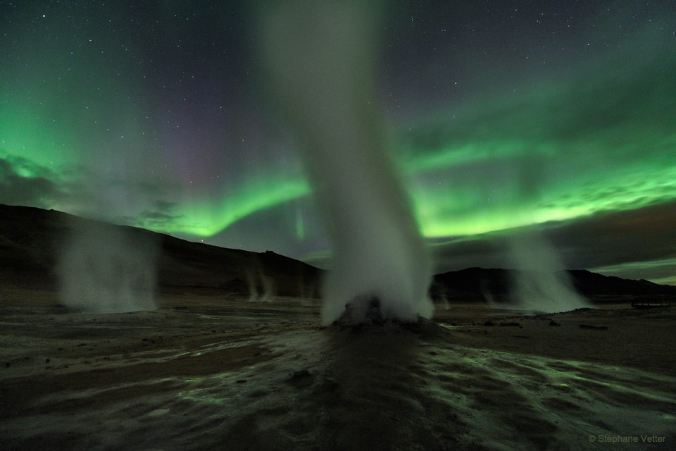 这张特色图片显示了冰岛地热活跃区Hverir的几个独立喷口冒出的蒸汽。绿色极光在背景中肆虐。有关更多详细信息，请参阅说明。