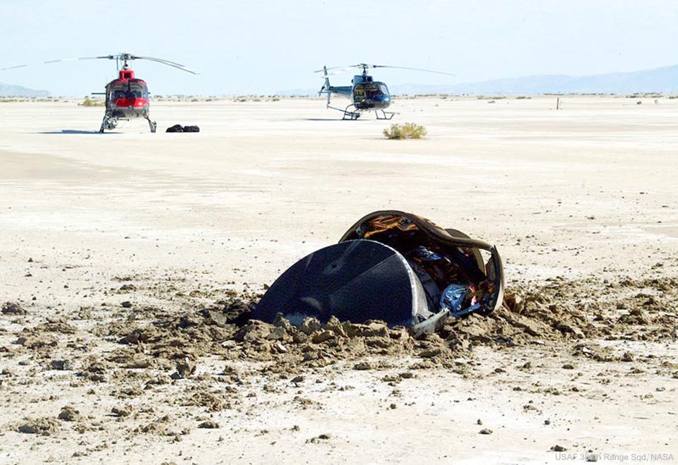 这张特色图片显示了NASA创世纪号任务中的飞碟嵌入沙子中，两架直升机在远处可见。有关更多详细信息，请参阅说明。
