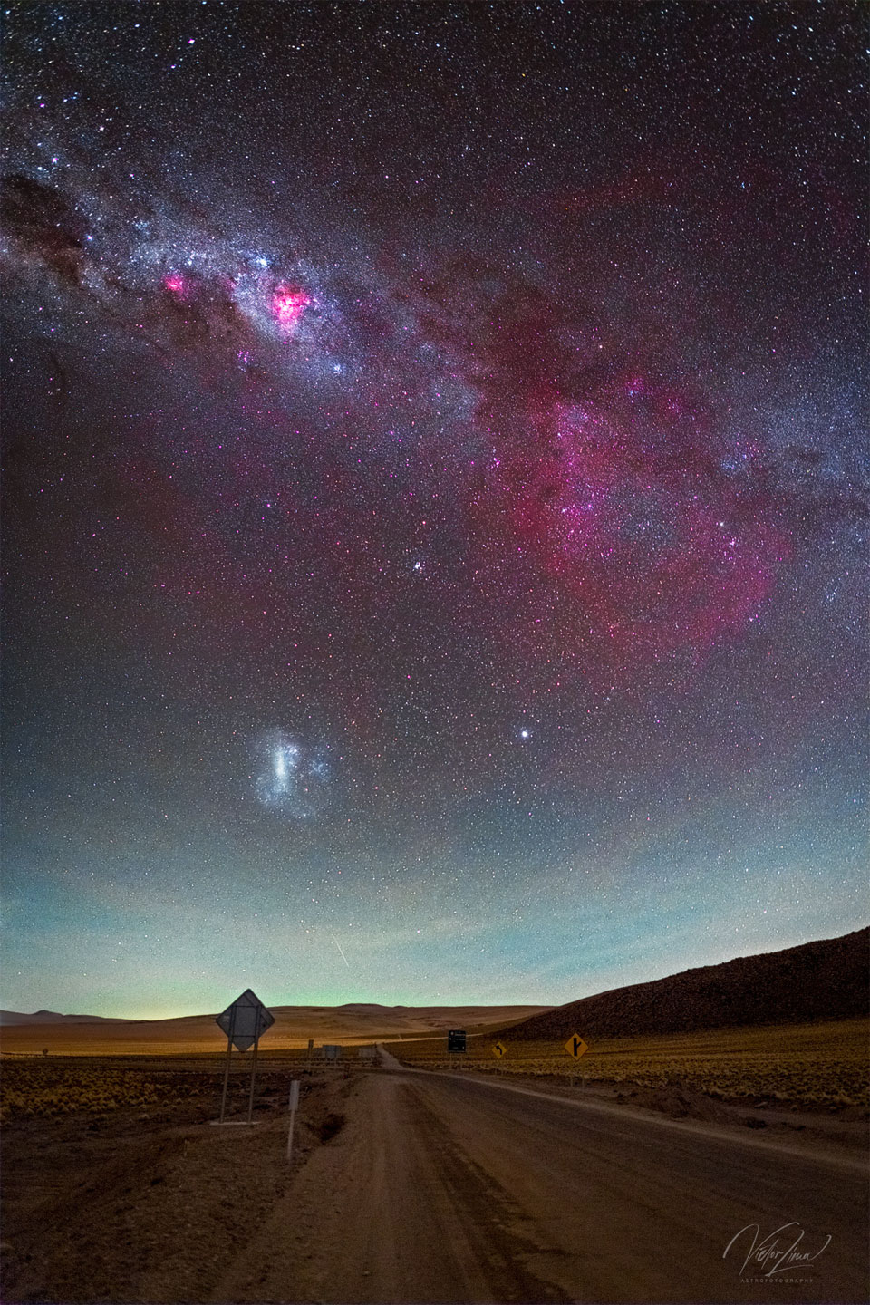 这张特色图片展示了一个宏伟的天空景观，前景是一条棕色的沙漠道路，天空包含了银河系的星系带，在右侧有一个大的红色辉光，这是昏暗的甘姆星云。LMC星系也可见。有关更多详细信息，请参阅说明。
