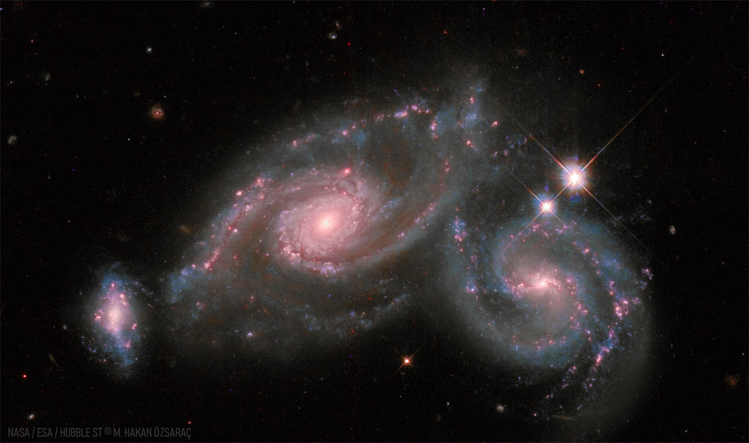 图中两个螺旋星系紧挨着，最左边是一个较小的扭曲星系。有关更多详细信息，请参阅说明。