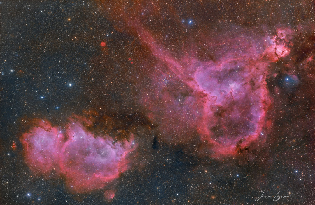 两个红色的发射星云出现在一个黑暗但色彩斑斓的星空前。灵魂星云在左下方，而心脏星云在右上方。有关更多详细信息，请参阅说明。