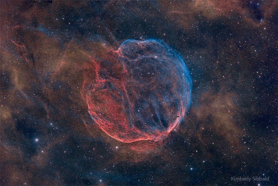 在星空的背景下，呈现出一个近乎球形的弦状星云。星云呈蓝色和红色。有关更多详细信息，请参阅说明。