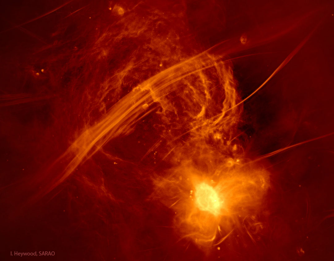 我们银河系中心的一幅伪色的红黄相间的射电图像显示，条纹上方有黄色的射电弧线，还有一个包含银河系中心黑洞的明亮茧状物。有关更多详细信息，请参阅说明。