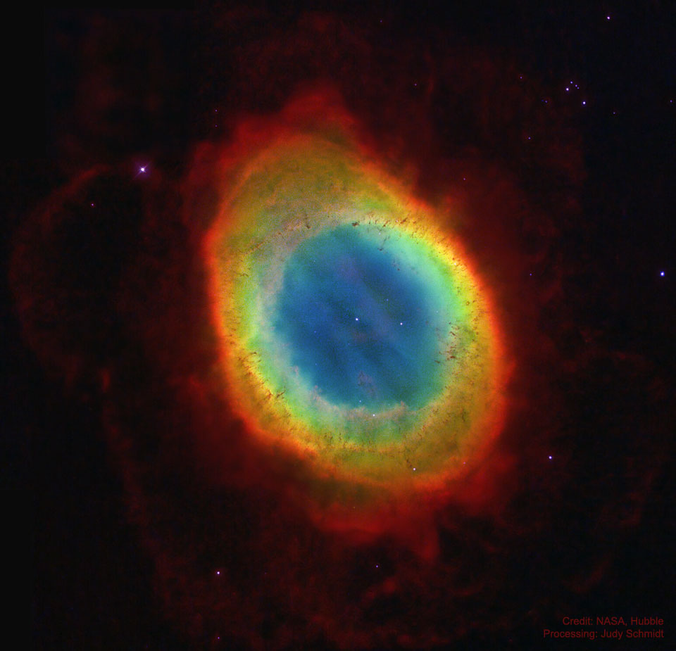 一个彩色的椭圆形星云显示在一个稀疏的星场中。明亮的椭圆形周围环绕着微弱的红色星云。在椭圆的中心可以看到一颗相对明亮的恒星。有关更多详细信息，请参阅说明。