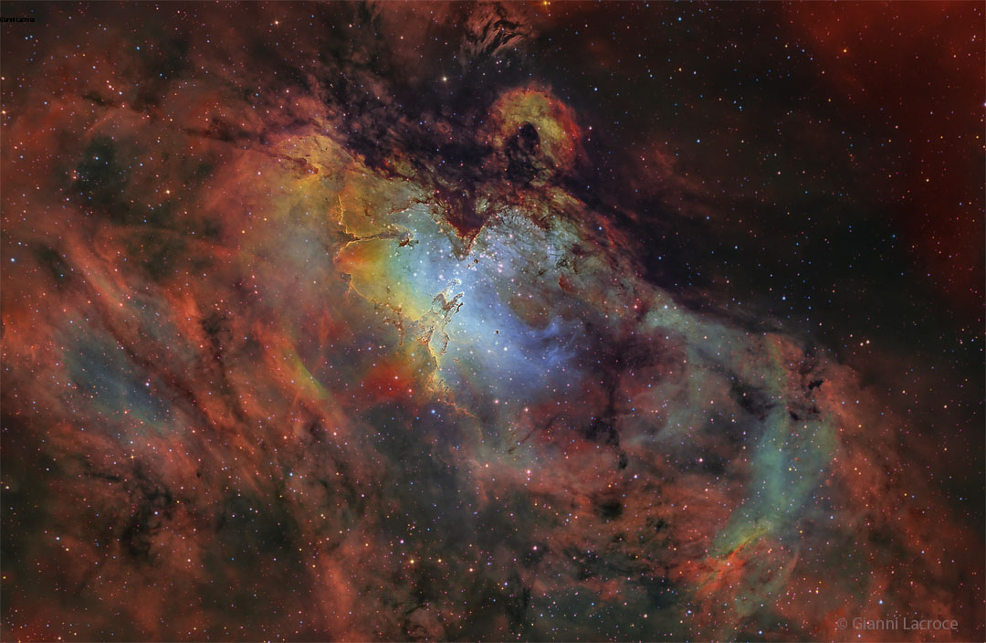 以许多科学指定的颜色呈现的鹰状星云的深场影像。星云周围的区域呈红色，但中心呈蓝色，可见不寻常的柱状物。有关更多详细信息，请参阅说明。
