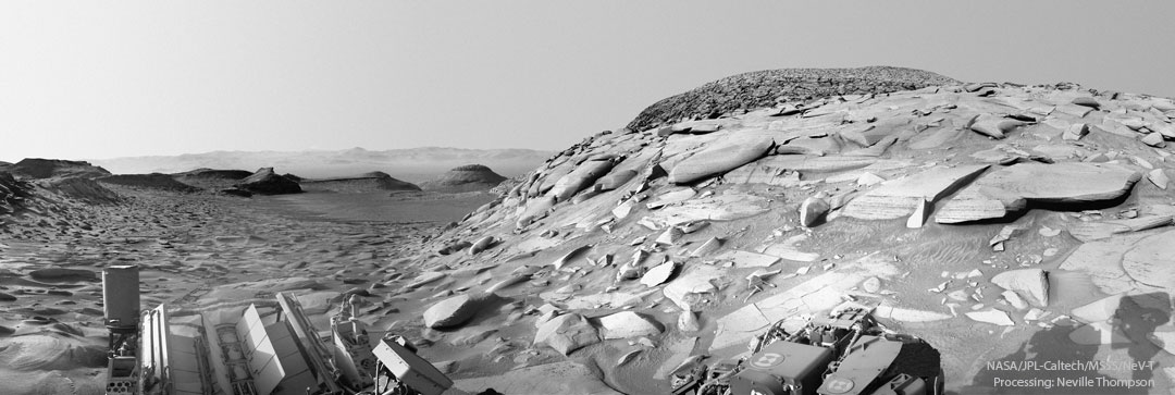 好奇号火星车在火星上拍摄的一幅黑白照片。可以看到许多岩石和山丘，右边可以看到一座包含许多异常平坦岩石的山丘。有关更多详细信息，请参阅说明。