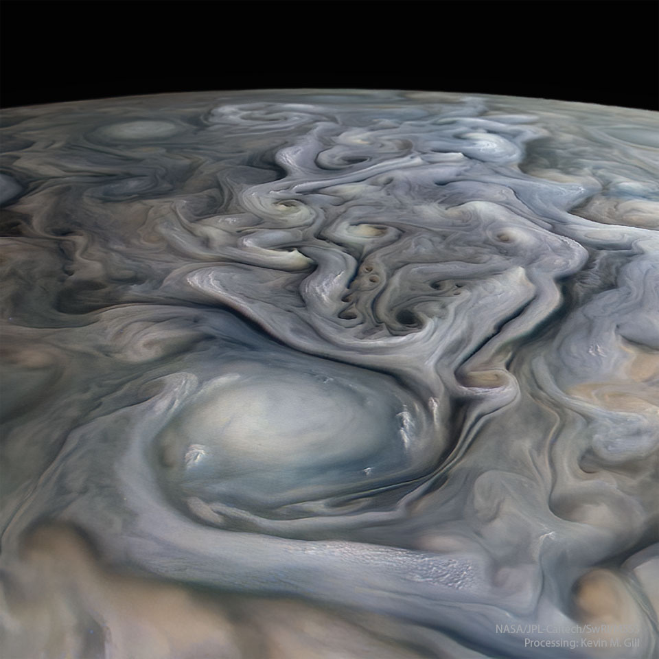 朱诺号宇宙飞船近距离飞掠木星时拍摄的云顶。在前景中可以看到一大片白色椭圆形云，而后面可以看到许多柔和颜色的漩涡。背景是漆黑的夜空。有关更多详细信息，请参阅说明。