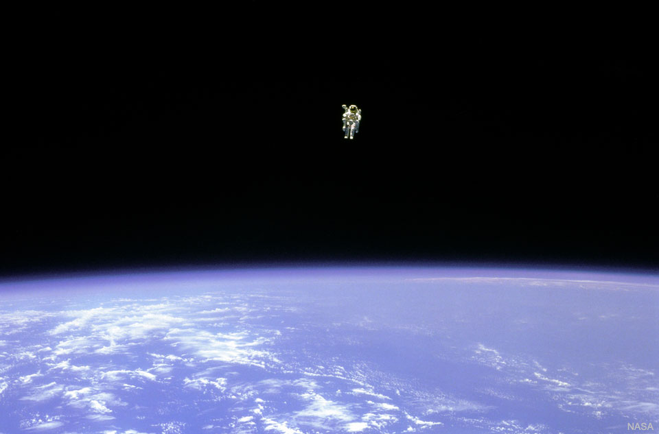 有人看到一名宇航员在地球上空盘旋。在图像的顶部，可以看到宇航员在黑暗的太空中。在图像的下半部分，地球是明亮的蓝色，有白云。有关更多详细信息，请参阅说明。