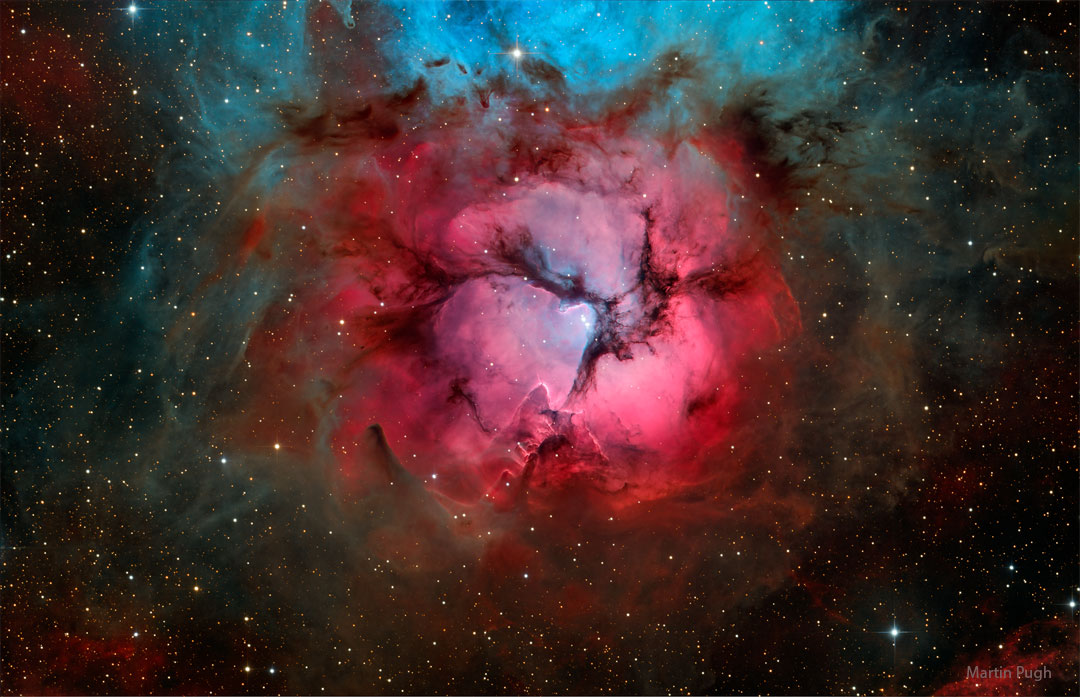 照片中是一个明亮的红色气体星云，中间有三条黑暗的尘埃带。星云的顶部呈现蓝色。有关更多详细信息，请参阅说明。