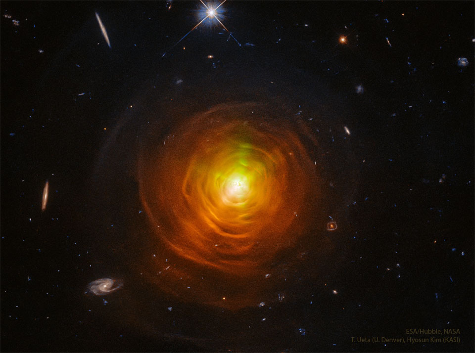 一颗被橙色贝壳和弧线包围的恒星坐落在黑暗星场的中心。在边缘可以看到来自遥远宇宙的星系。关更多详细信息，请参阅说明。