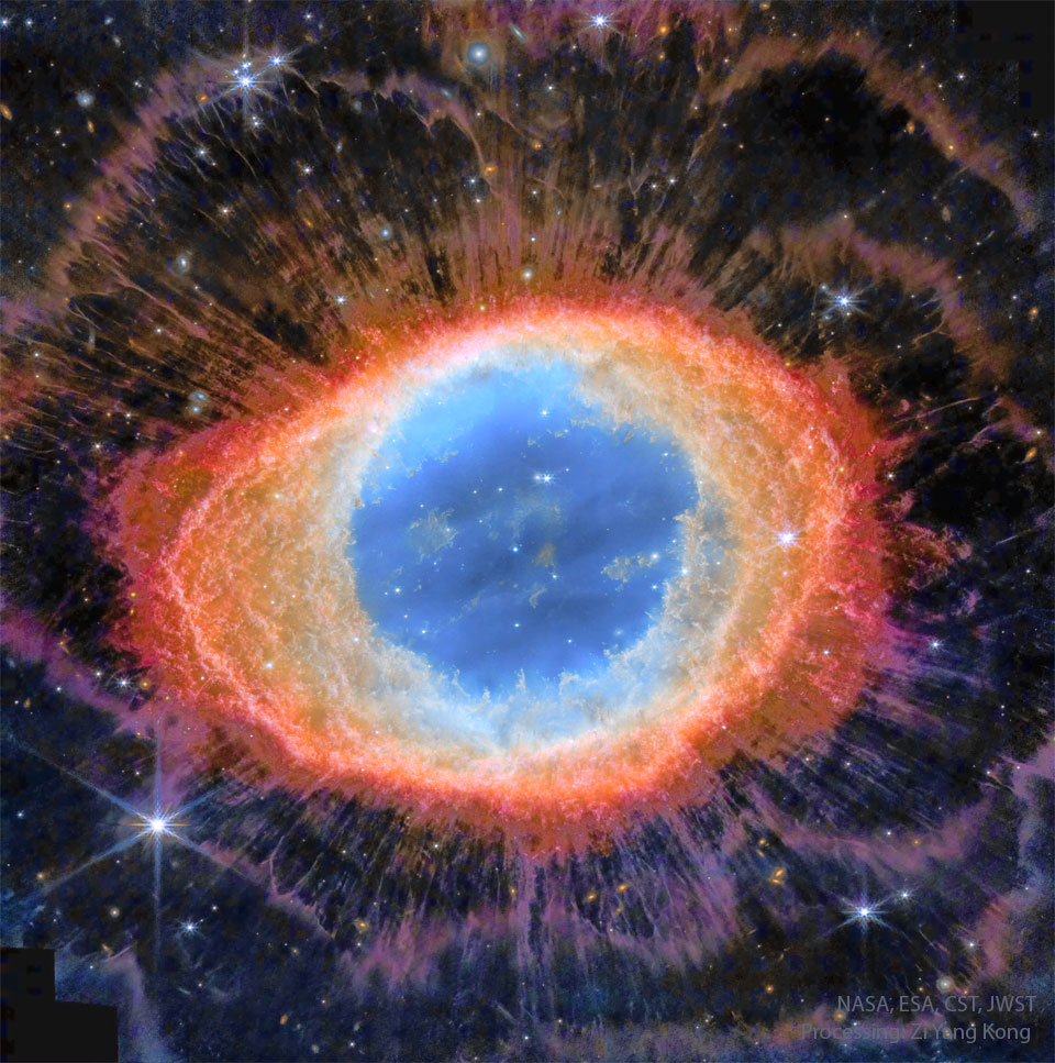 椭圆形星云以假色呈现。星云的中心呈蓝色，边缘呈橙色和红色，橙色和紫色的细丝延伸到画面的边缘。在整个画面中可以看到恒星。有关更多详细信息，请参阅说明。