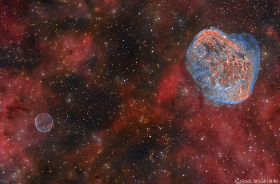 在黑暗的星场前，可以看到红色的发光气体。右上方是一个蓝色和红色的复杂丝状星云。左下角是一个简单的蓝色圆形星云。有关更多详细信息，请参阅说明。