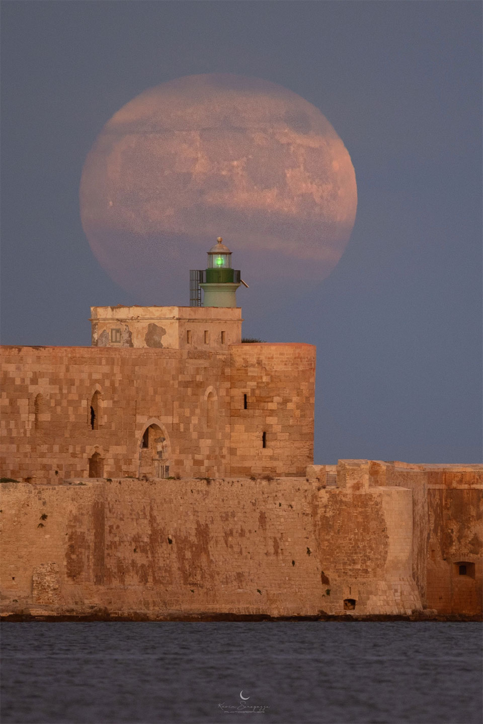 一轮大月亮出现在一座历史悠久的石头建筑后面。有关更多详细信息，请参阅说明。