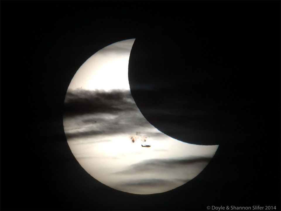图为日偏食。太阳的前面是太阳黑子、月亮、云和一架飞机。有关更多详细信息，请参阅说明。