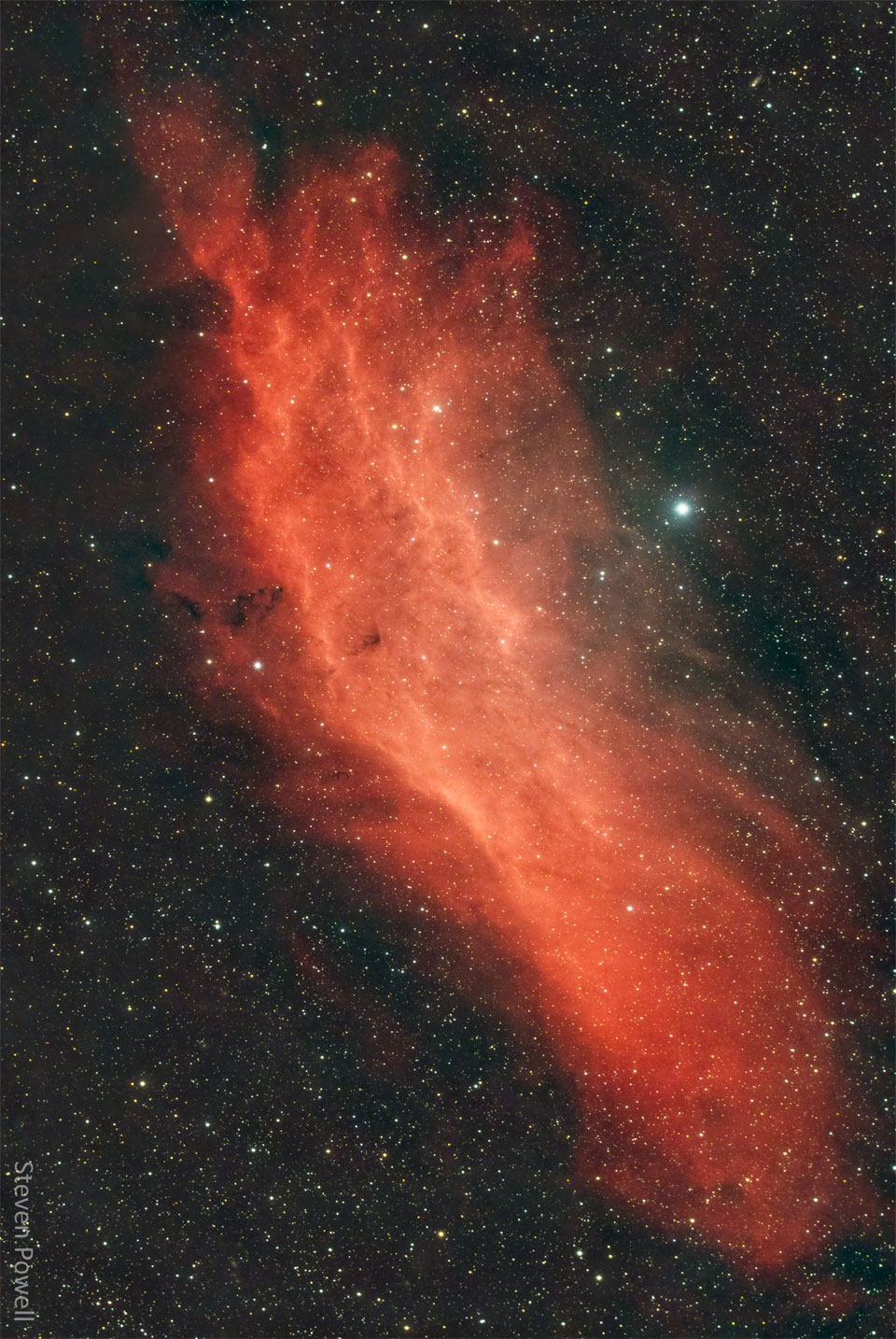 一个红色的气态星云显示在黑暗的星场前面。星云的形状类似于美国的加州。有关更多详细信息，请参阅说明。
