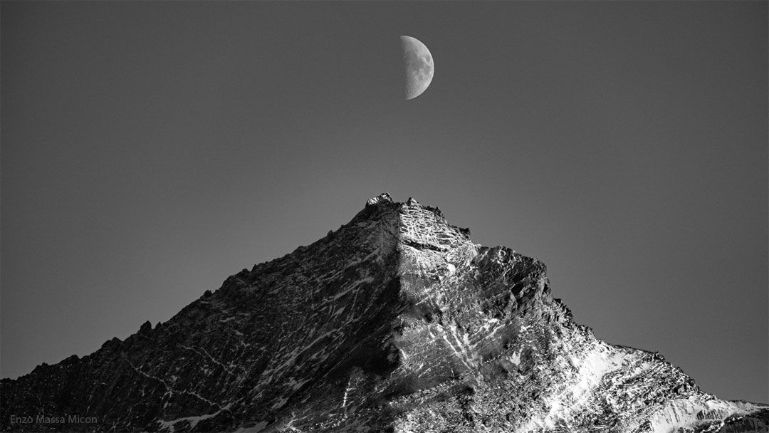 这是一张月球和一座山的黑白照片。两者都有一半被太阳照亮，另一半被阴影遮蔽。上弦月就在山顶的正上方。有关更多详细信息，请参阅说明。