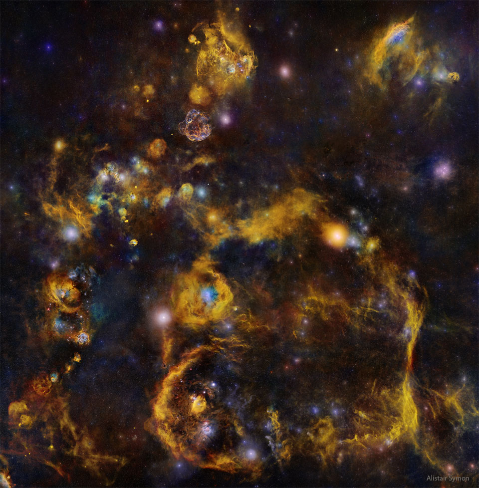 一张极深的夜空影像显示了许多恒星和星云。许多明亮的星云似乎是由微弱的橙色细丝连接起来的。有关更多详细信息，请参阅说明。