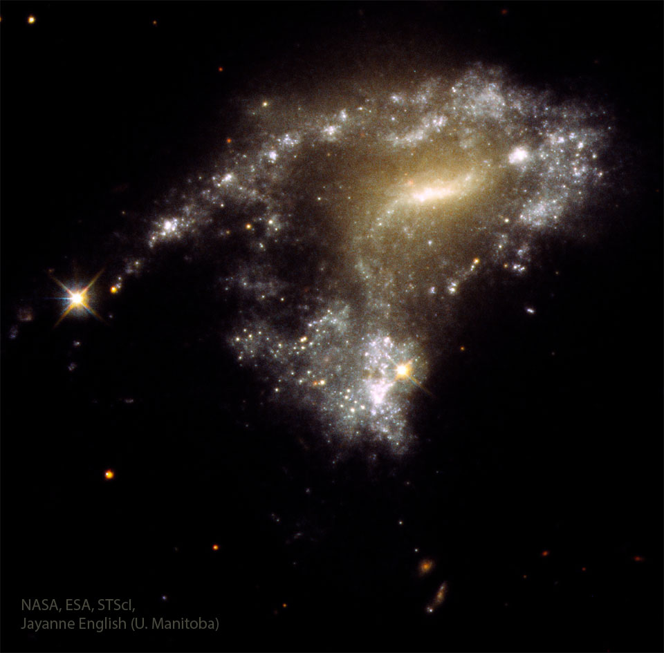 图中显示的是一个扭曲的星系，左边是一串逐渐消失的恒星。有关更多详细信息，请参阅说明。