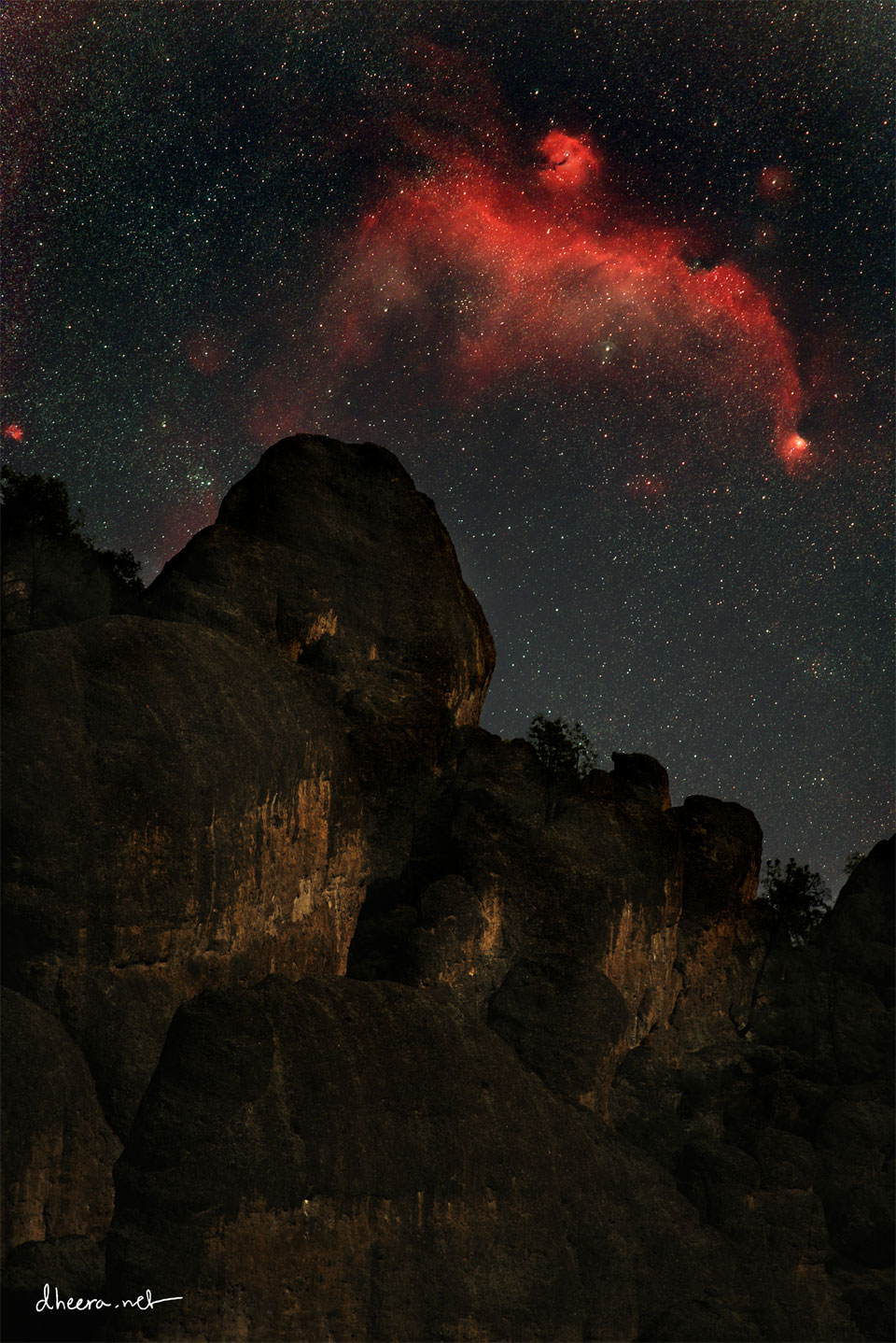 在一座岩石峰上方，可以看到黑暗星空中的红色星云。这个星云看起来像一只飞鸟。有关更多详细信息，请参阅说明。