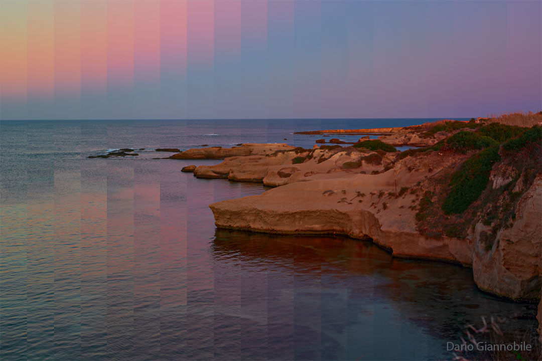 图片显示了岩石海岸线，右侧是陆地，左侧是水域。上方的天空显示出不同寻常的像素化和彩色垂直带。有关更多详细信息，请参阅说明。